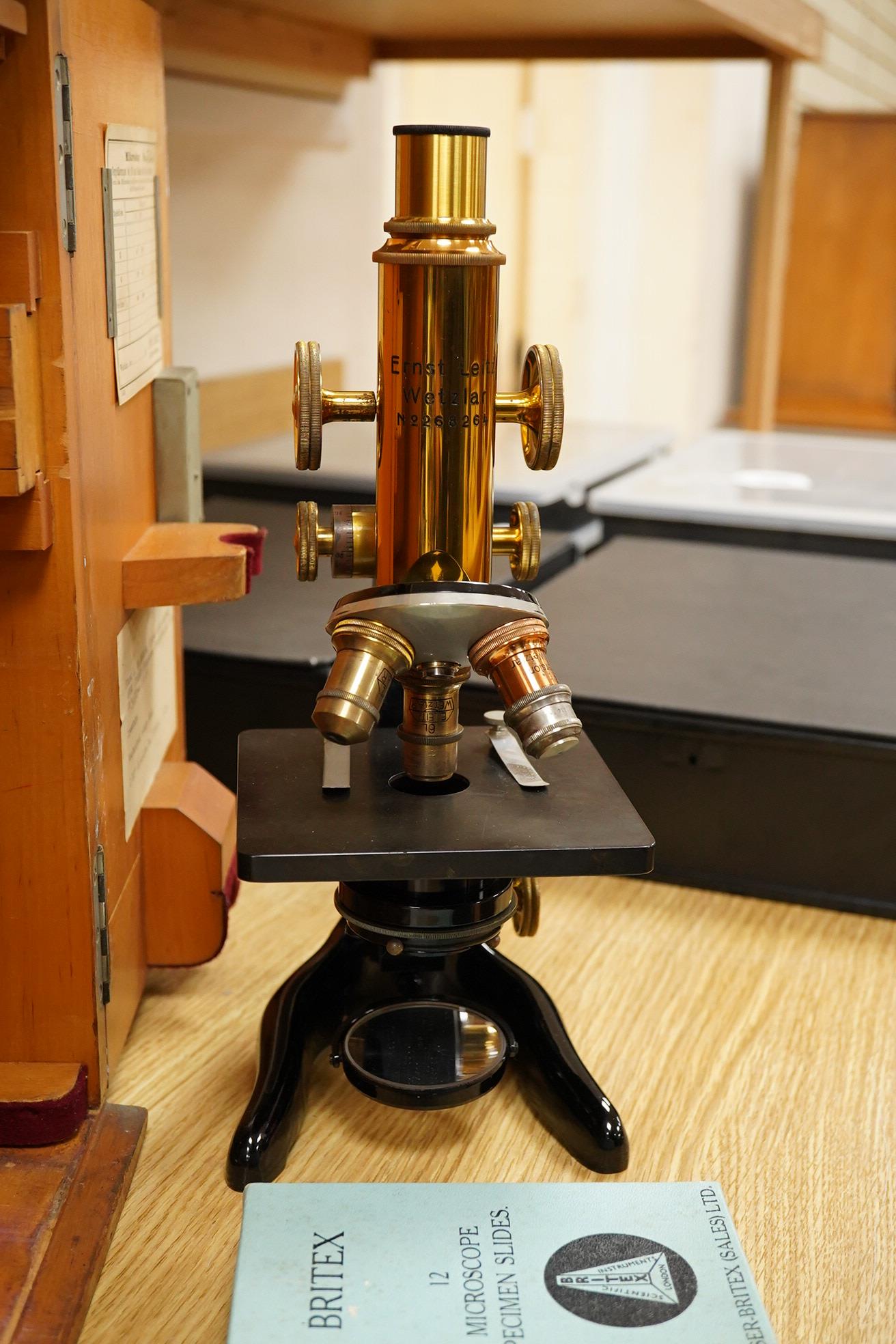 An early 20th century teak cased Ernst Leitz, Wetzlar brass and cast iron monocular microscope, serial no. 268264, with fitted interior to the case and card box of specimen slides, case dimensions; 36cm high, 19cm wide,